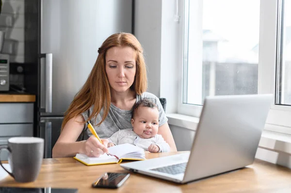 Uma jovem mãe usando laptop para trabalho remoto — Fotografia de Stock