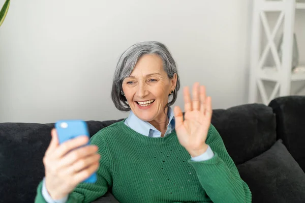 Positive senior lady is waving at the phone — Stock Photo, Image