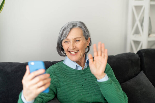 Positive senior lady is waving at the phone