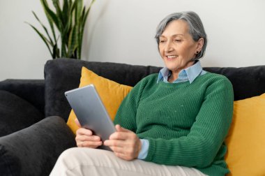 Sarı yastıklı bir kanepede oturan yaşlı bayan.