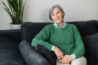 Oturma odasındaki kanepede oturan yaşlı bayan.