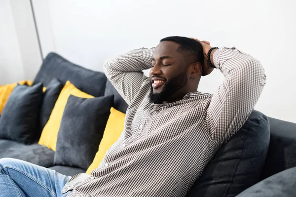 Rento hymyilevä Afro American nauttia elämästä istuu sohvalla — kuvapankkivalokuva