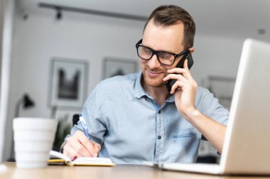 Adamın biri masada otururken dizüstü bilgisayar kullanıyor.