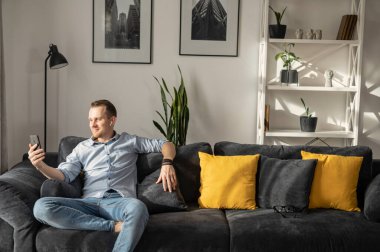 Akıllı telefonlu bir adam kanepede oturur.