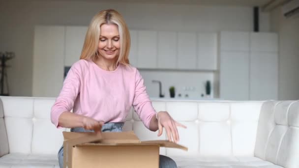 Женщина средних лет распаковывает коробку с вещами — стоковое видео