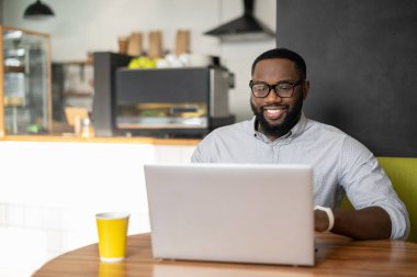 Afro-Amerikalı bir adam rahat bir kafede masada oturuyor.