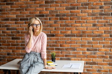 Olgun sarışın iş kadını cep telefonuyla konuşuyor.