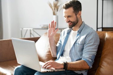 Yakışıklı, sakallı, sıradan bir tişört giyen, dizüstü bilgisayar kullanan.