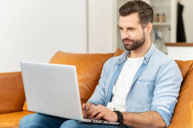 Yakışıklı, sakallı, sıradan bir tişört giyen, dizüstü bilgisayar kullanan.