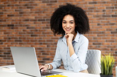 Genç iş kadını bilgisayarın önünde oturuyor ve kameraya poz veriyor.