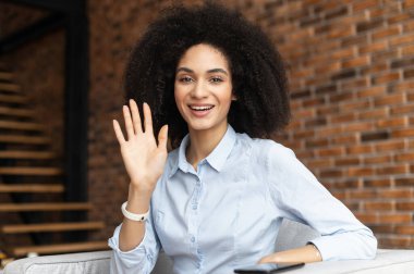 Afrikalı Amerikalı ofis çalışanı kameraya el sallıyor.