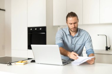 Ciddi bir iş adamı dizüstü bilgisayarının başında oturmuş, internette çalışıyor ve belgeleri okuyor.