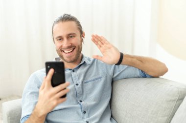 Pozitif genç adam kanepede oturup telefonda konuşuyor.