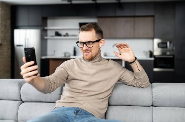 Yakışıklı, samimi bir adam telefonu elinde tutuyor ve onu videoyla selamlıyor.