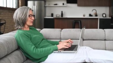 Olgun yaşlı kadın evde dizüstü bilgisayar kullanıyor.