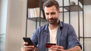 Sıradan giyinen genç sakallı hippi cep telefonu ve kredi kartı kullanıyor.
