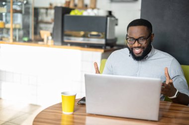 Afro-Amerikalı bir adam rahat bir kafede masada oturuyor.