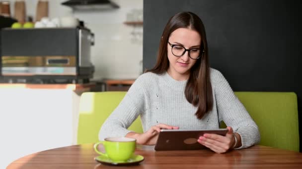 Egy fiatal nő digitális tablettel a kávézóban. — Stock videók