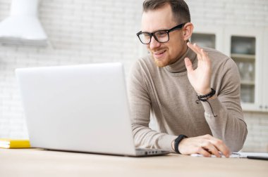 Genç sakallı hippi dizüstü bilgisayarına el sallıyor.