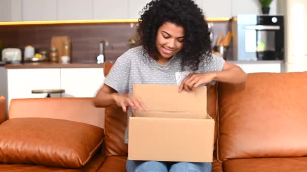 Overjoyed young African-American female unpacking cardboard parcel box — Stock Video