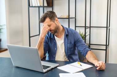 Yorgun işadamı dizüstü bilgisayarın başında oturuyor ve belgeleri okuyor.