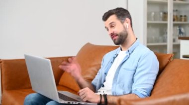 Sıradan bir tişört giyen odaklanmış bir adam video görüşmesi için dizüstü bilgisayar kullanıyor.