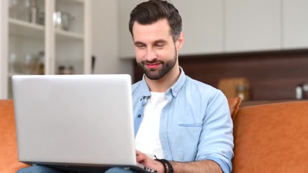 Ein fokussierter Mann mit lässigem Hemd und Laptop sitzt zu Hause — Stockvideo