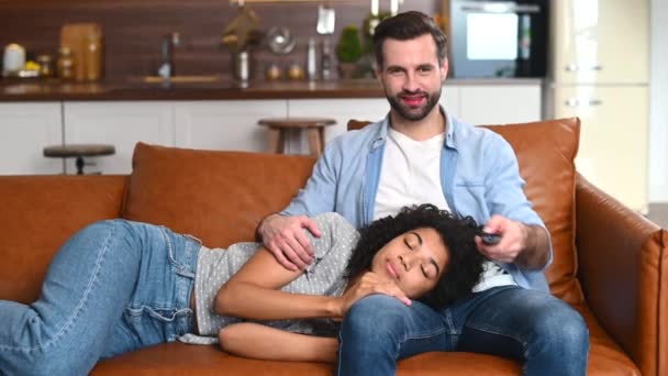 Мультирасовая пара отдыхает на диване, смотрит кино — стоковое видео