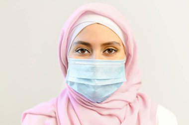 Başörtüsü ve tıbbi maske takan genç bir müslüman kadın.