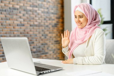 Başörtüsü takan genç Müslüman bir kadın video araması için laptop kullanıyor.