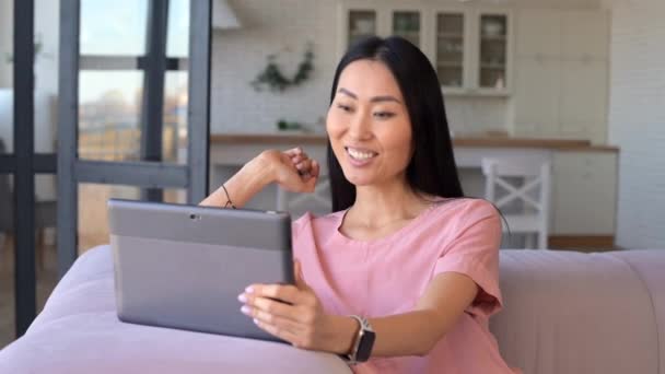 Uma jovem mulher asiática alegre está usando um tablet digital para chamada de vídeo — Vídeo de Stock