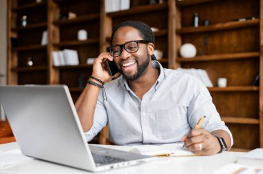 Laptop kullanan ve telefonla konuşan Afro-Amerikalı bir adam.