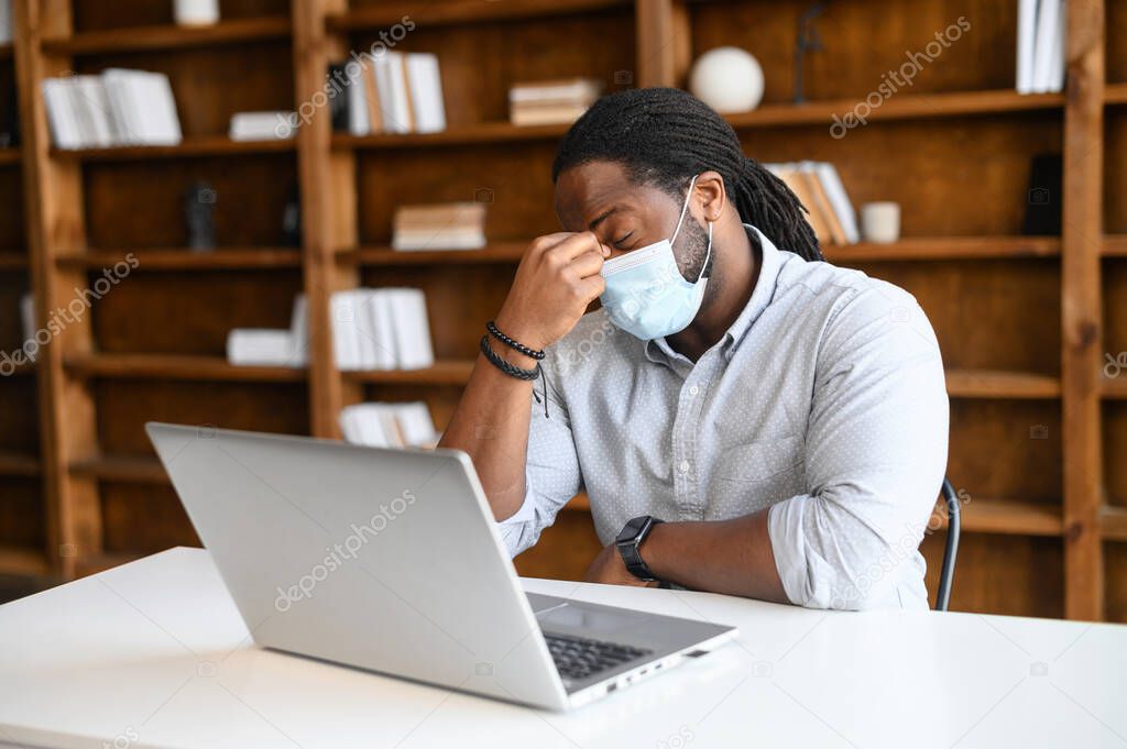 An African-American guy wearing medical mask using a laptop indoor