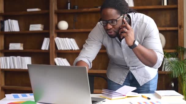 Young African American male employee using a laptop and smartphone — Stock Video