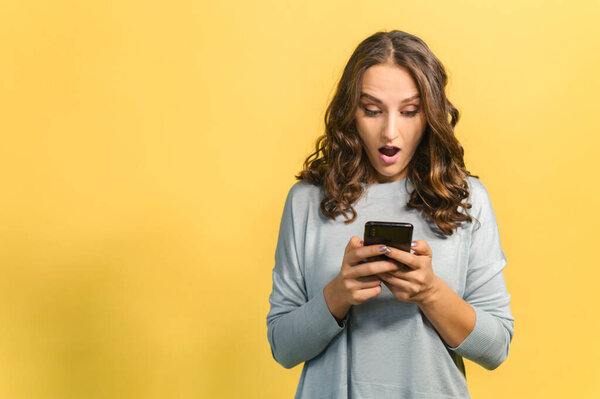 Шокированная женщина смотрит на экран смартфона, изолированный на желтый