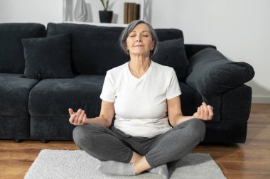 Yaşlı gri saçlı kadın evde yoga yapıyor.