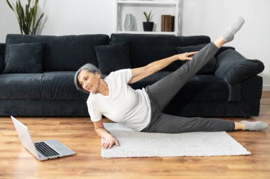 Yaşlı, kır saçlı kadın evde egzersiz yapıyor.