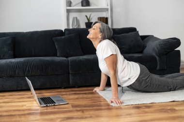 Yaşlı gri saçlı kadın evde yoga yapıyor.