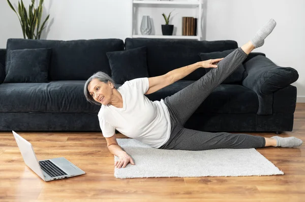 Yaşlı, kır saçlı kadın evde egzersiz yapıyor.