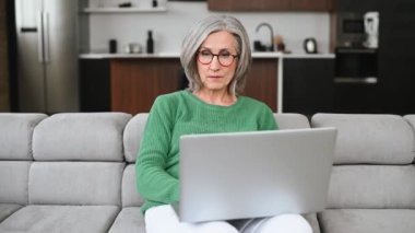 Olgun yaşlı kadın evde dizüstü bilgisayar kullanıyor.