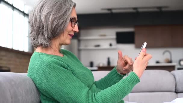 Volwassen senior vrouw is met behulp van een smartphone thuis — Stockvideo