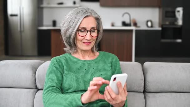 Maturo anziana donna sta utilizzando uno smartphone a casa — Video Stock