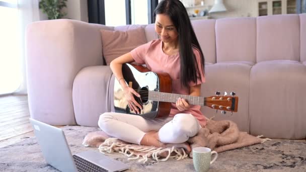 一位年轻貌美的亚洲女人正在家里弹吉他 — 图库视频影像