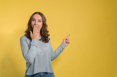 Genç ve çekici bir kadın boş bir yeri işaret ediyor, sarıda izole edilmiş.