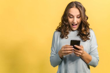 Akıllı telefon kullanan genç ve çekici bir kadın, sarıda izole edilmiş.