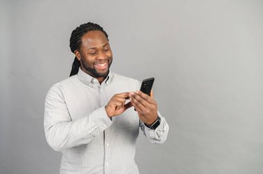 Gri yolda izole edilmiş akıllı telefonlu bir adamla gülümseyen Afro-Amerikalı.