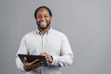 Elinde dijital tablet tutan gülümseyen Afro-Amerikan adam gri üzerinde izole edilmiş.