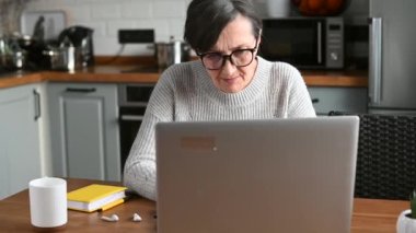 Üst düzey kadın evde dizüstü bilgisayar kullanıyor, uzaktan çalışıyor.