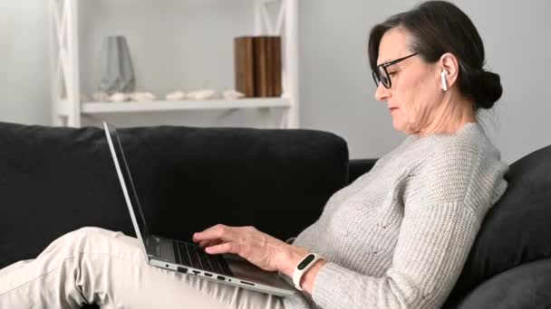 Idősebb nő, aki laptopot használ otthon, távolról dolgozik — Stock videók