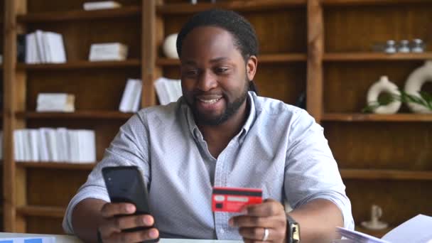 Afrikalı Amerikalı adamın elinde akıllı telefon ve kredi kartı var. — Stok video